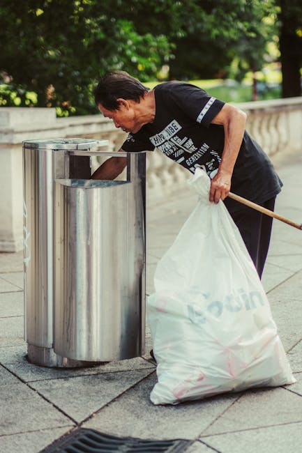 In the foreground, a pile of assorted waste materials includes a large, empty cardboard box with visible corrugated edges, stacked slightly askew on a concrete surface. Next to it, there are several t